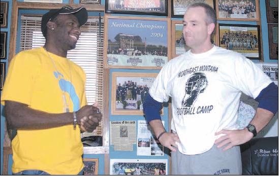 Derrick Atkins, left, and Dickinson State track and field coach Pete Stanton speak in Stanton’s office at the DSU athletic department. Photos of the Blue Hawks’ national track and field championships, along with photos of Atkins’ recent accomplishments, adorn Stanton’s wall. 